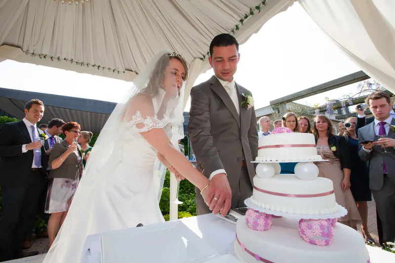 Anouk en Edgar snijden de taart aan onder een witte tent