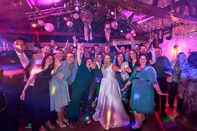 Bruidspaar en gasten dansen met de armen omhoog