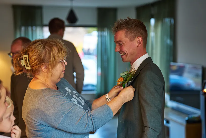 Glenn lacht terwijl de corsage op zijn jasje wordt gespeld