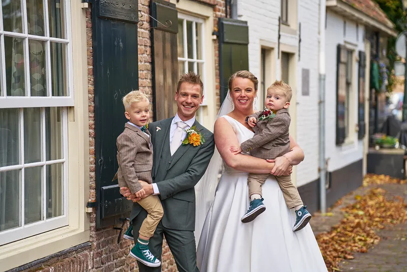 Karlijn en Glenn lachen met de kinderen op de arm voor een oude gevel