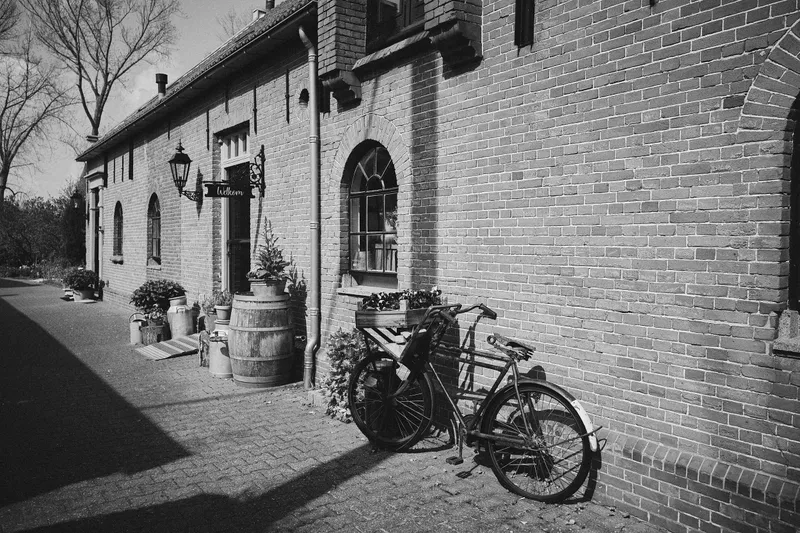De binnenplaats van Burgersdijk met een oude fiets tegen de bakstenen muur, zwart-wit