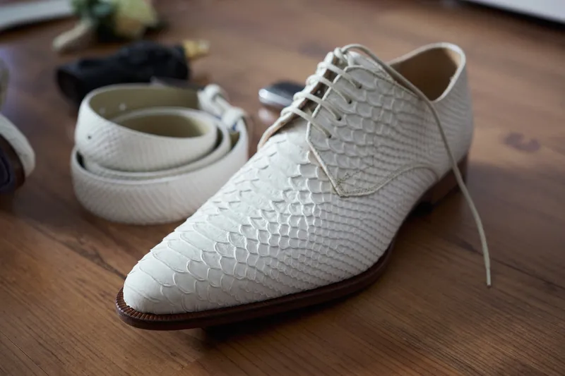 De witte schoenen van Cees en zijn riem op een houten tafel