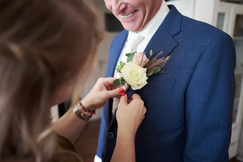 De dochter van Cees speldt de corsage op zijn blauwe pak