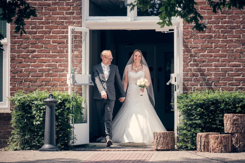 Ilja loopt arm in arm door de deur van het hotel naar buiten, op weg naar de ceremonie