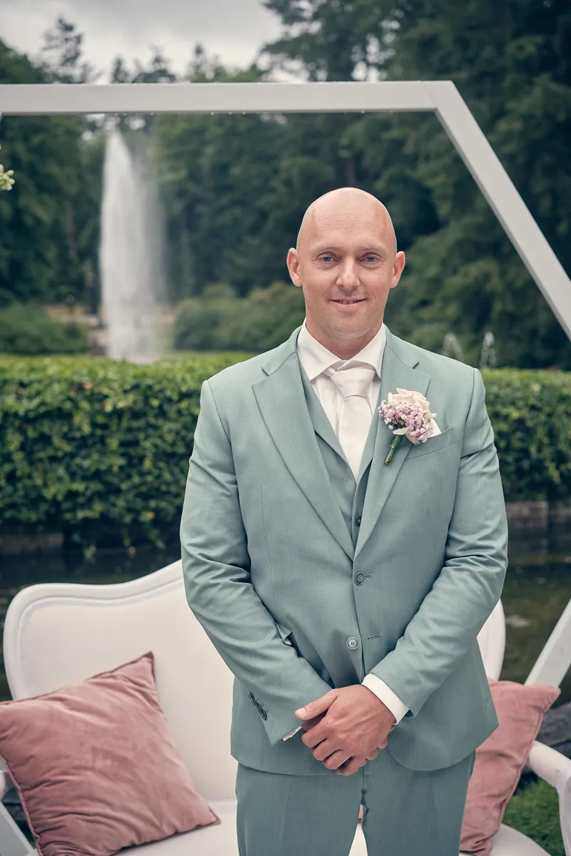 Dennis wacht onder de witte boog, met de fontein erachter