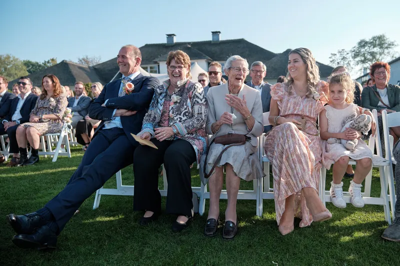 Gasten op witte stoelen op het gras, een man leunt achterover