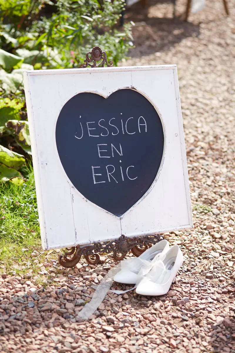 Een hartvormig bord met hun namen en witte schoenen op de grond