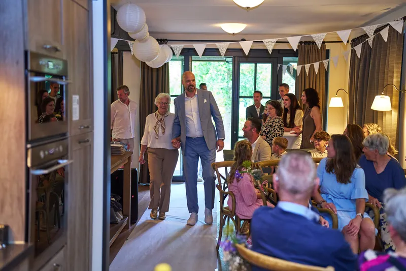 Jan komt binnen met zijn moeder, tussen de gasten in de woonkamer
