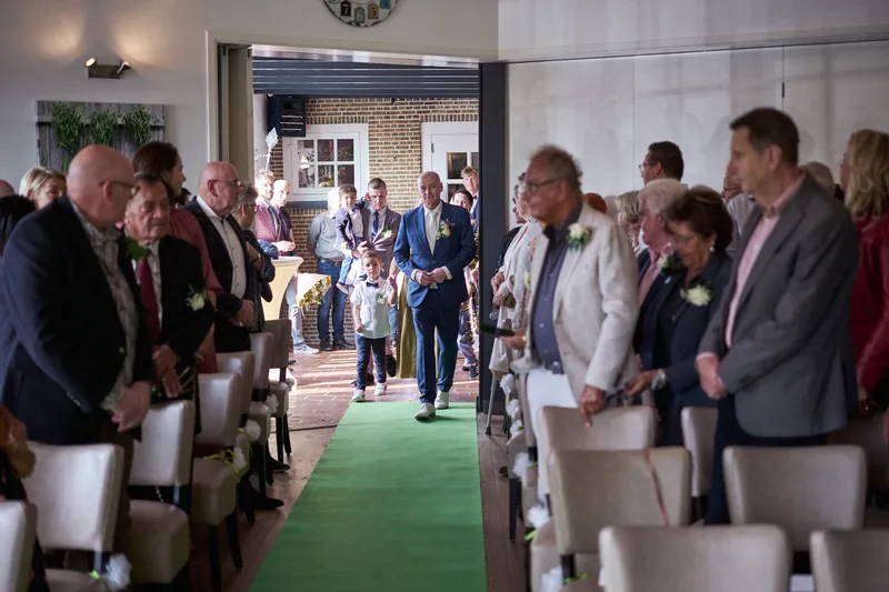 De gasten kijken om naar de groene loper waar het bruidspaar binnenkomt