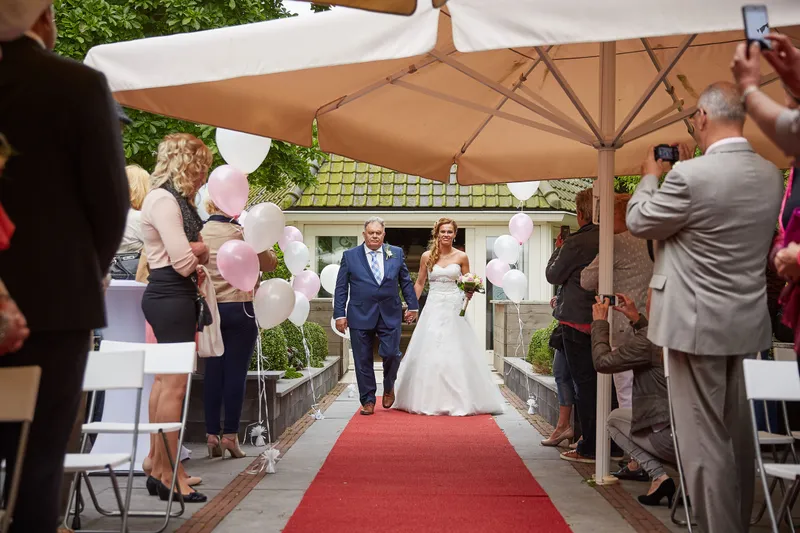 Trudy en Ron lopen over de rode loper onder de parasols