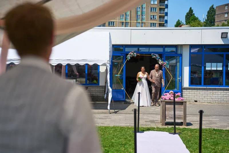 Felicia loopt aan de arm van haar vader van het clubhuis naar de tent