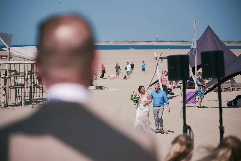 Mirjam loopt met haar broer over de loper naar de boog, met de zee erachter