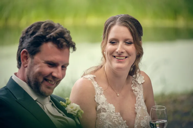 Fabian en Renée lachen samen tijdens de ceremonie, het water achter hen