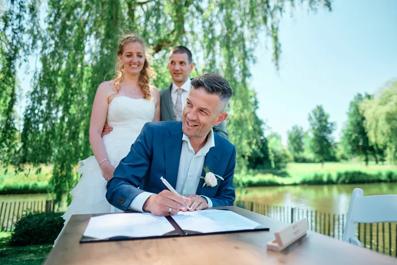 Een broer tekent als getuige, Ylona en Wouter erachter, met het water en de wilgen