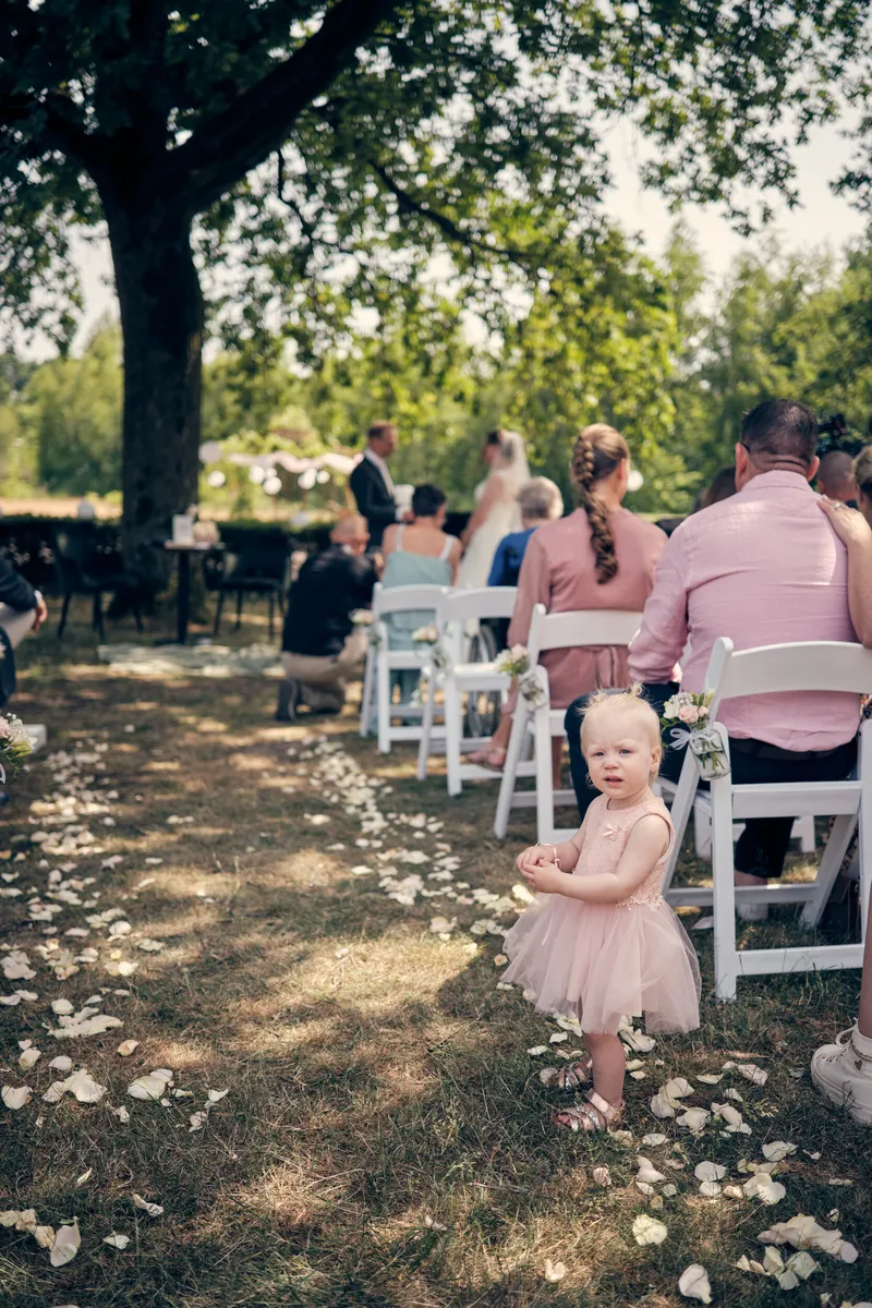 Een van de dochtertjes loopt in haar roze jurk over de bloemblaadjes tussen de witte stoelen