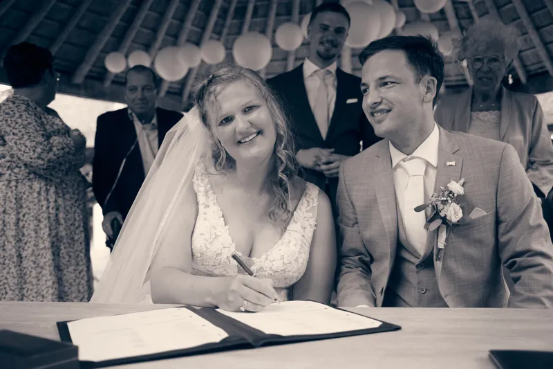 Zwart-wit: Julia en Rens lachen bij het tekenen van de trouwakte