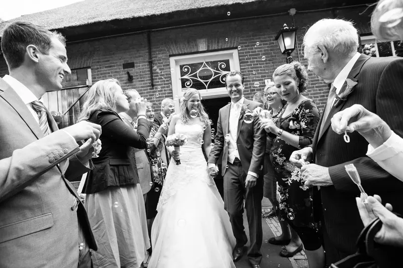 Gasten feliciteren het bruidspaar voor de boerderij, in zwart-wit