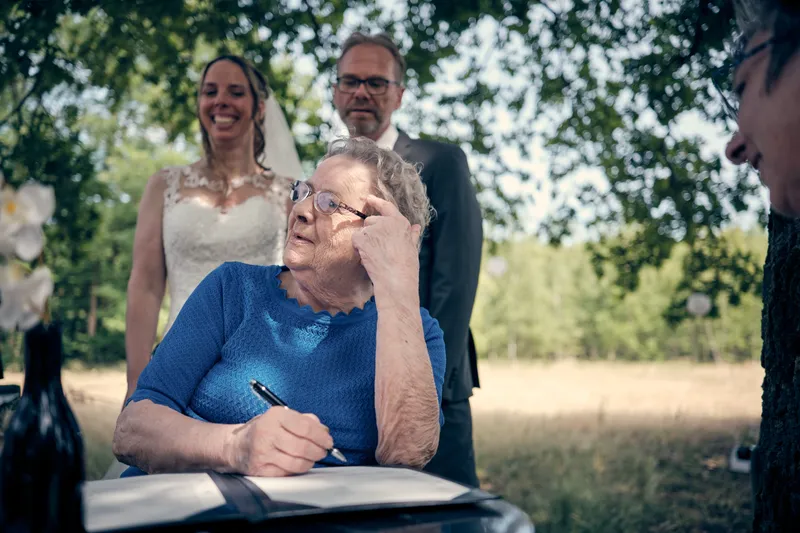 Oma van Ilja zet haar handtekening, het bruidspaar staat erachter