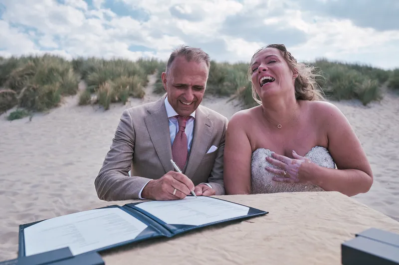 Jorg en Mirjam lachen terwijl ze tekenen, het duin erachter