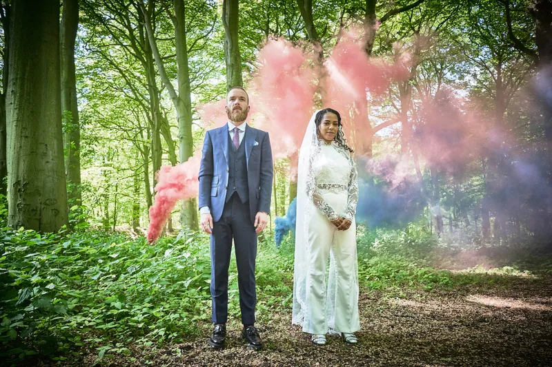 Frank en Jennifer staan tussen roze en blauwe rook in het bos
