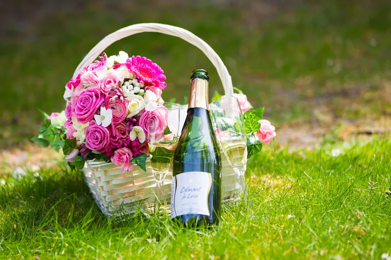Een mand met roze bloemen en een fles champagne in het gras