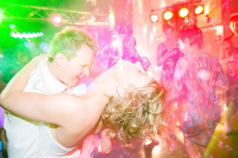 Het bruidspaar danst met de bruid achterover tussen zeepbellen in groen en roze licht