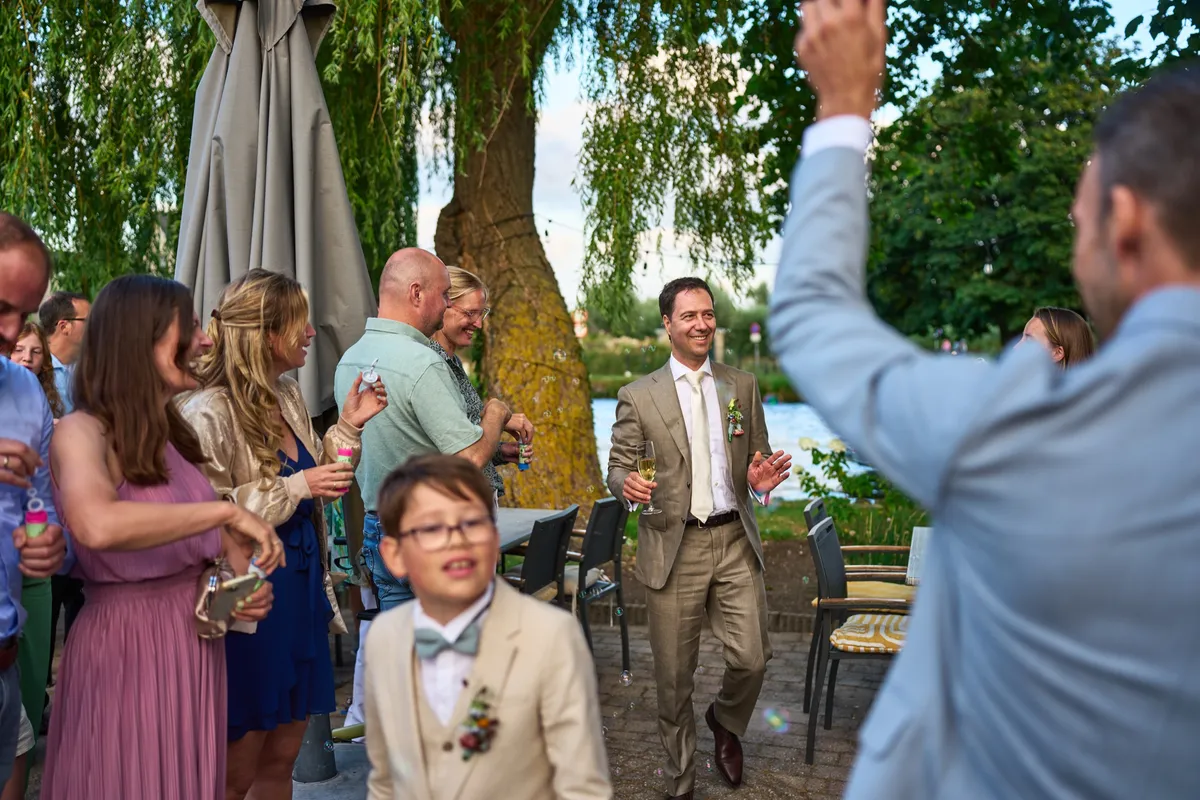 Rutger loopt lachend tussen de gasten met champagne op het terras bij de wilg
