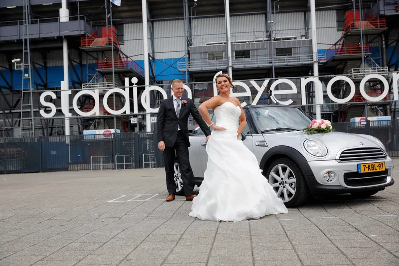 Het bruidspaar bij een zilveren Mini voor Stadion Feyenoord