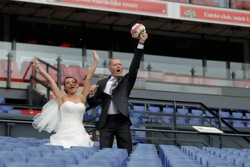 Het bruidspaar juicht met het boeket op de lege tribune van De Kuip