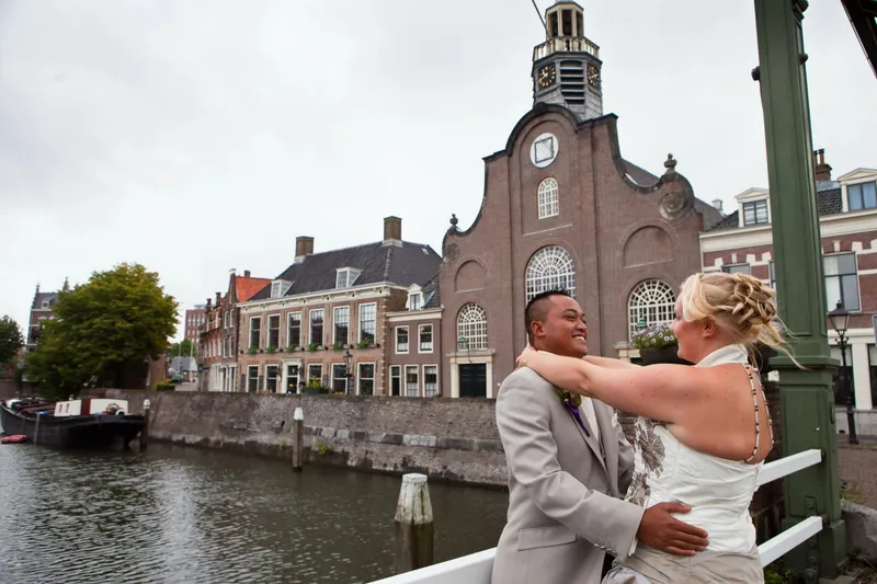 Het bruidspaar omhelst elkaar op een brug in Delfshaven, met de oude kerk op de achtergrond