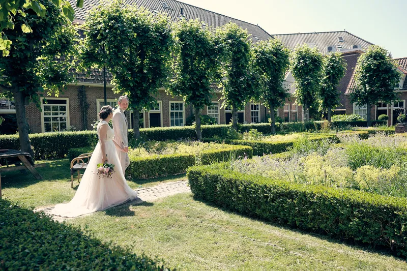 Evelien en Krijn lopen door een hofje met buxushagen en leilindes, vlak bij de Oostpoort