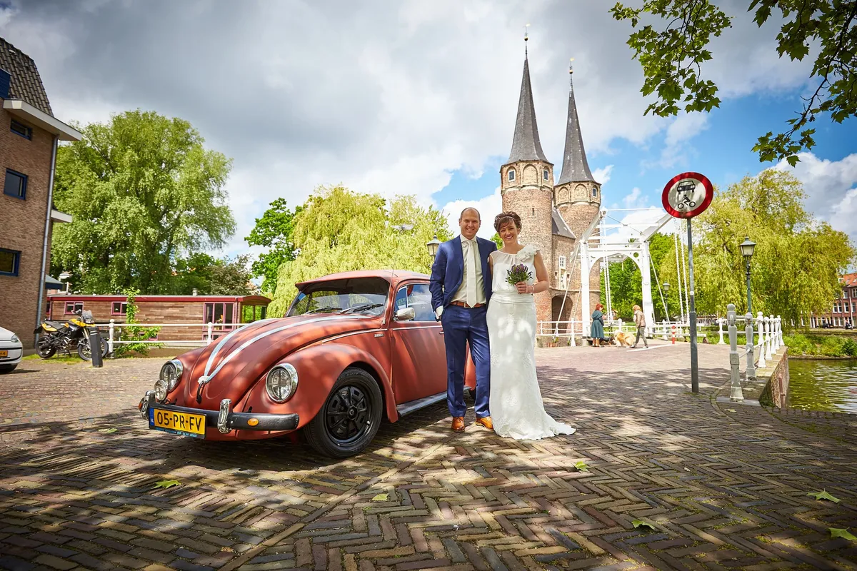 Marina en Erik bij de rode Kever, met de Oostpoort van Delft erachter