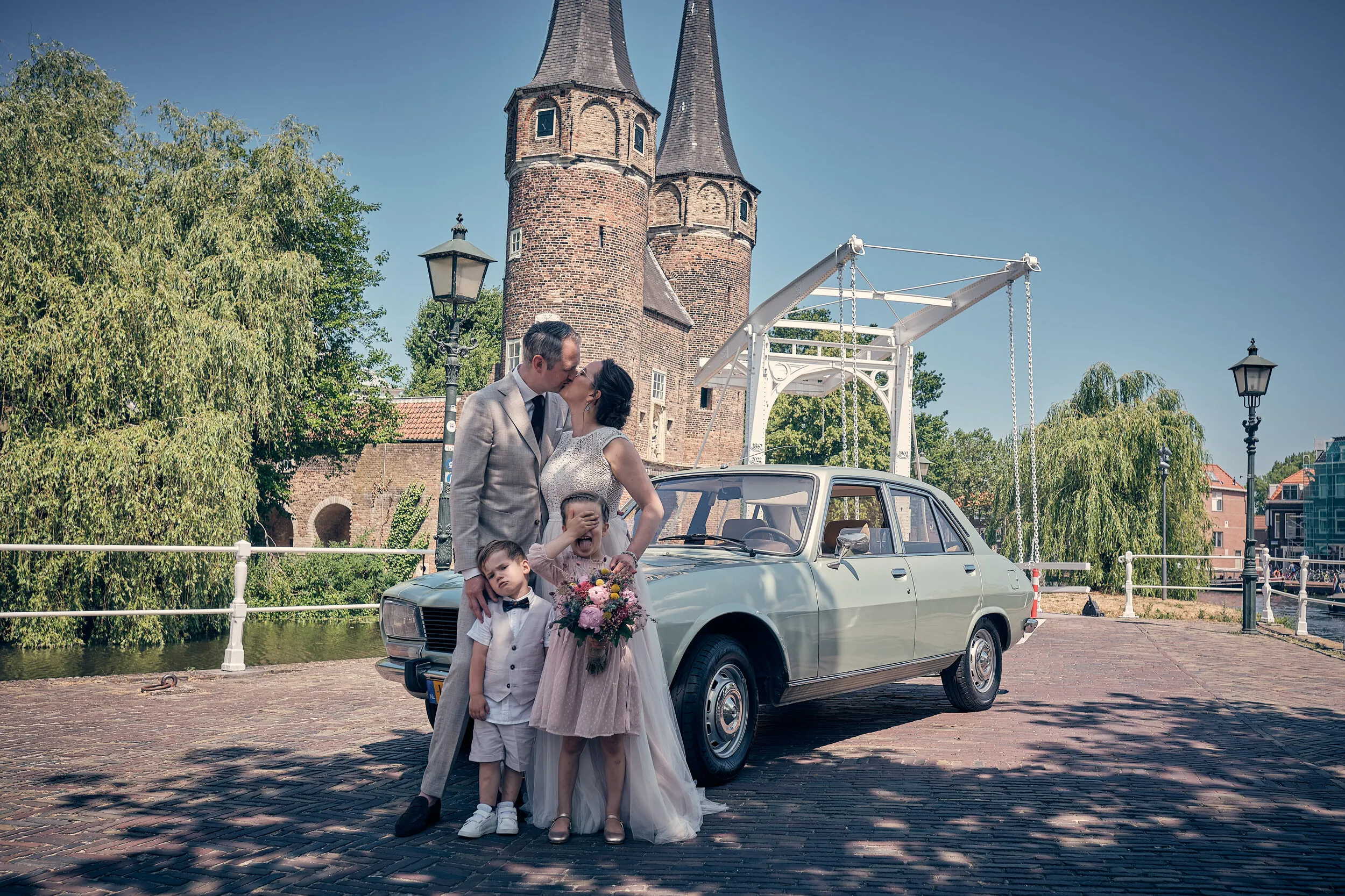Krijn en Evelien met hun kinderen bij de witte oude Peugeot op de brug voor de Oostpoort in Delft