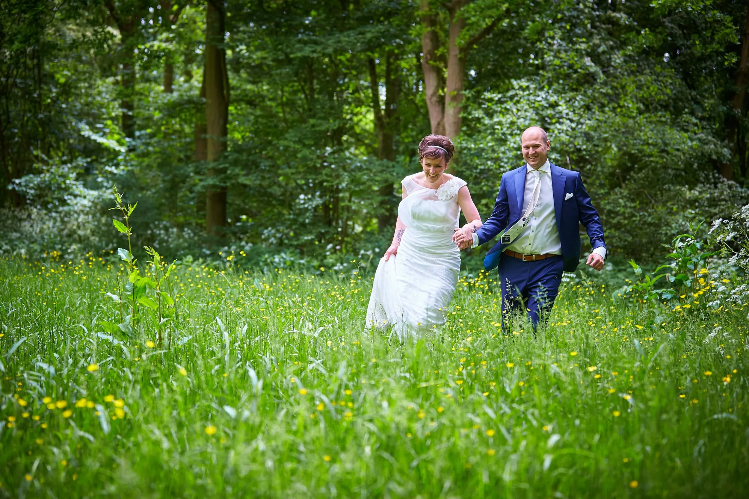 Marina en Erik rennen door het hoge gras met boterbloemen in de Delftse Hout