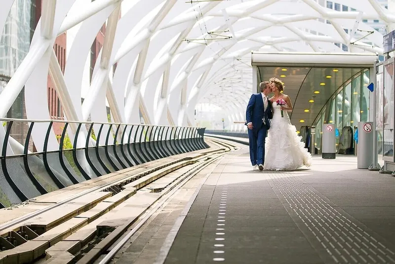 Het bruidspaar kust op de tramhalte in het Beatrixkwartier, onder een witte boogoverkapping