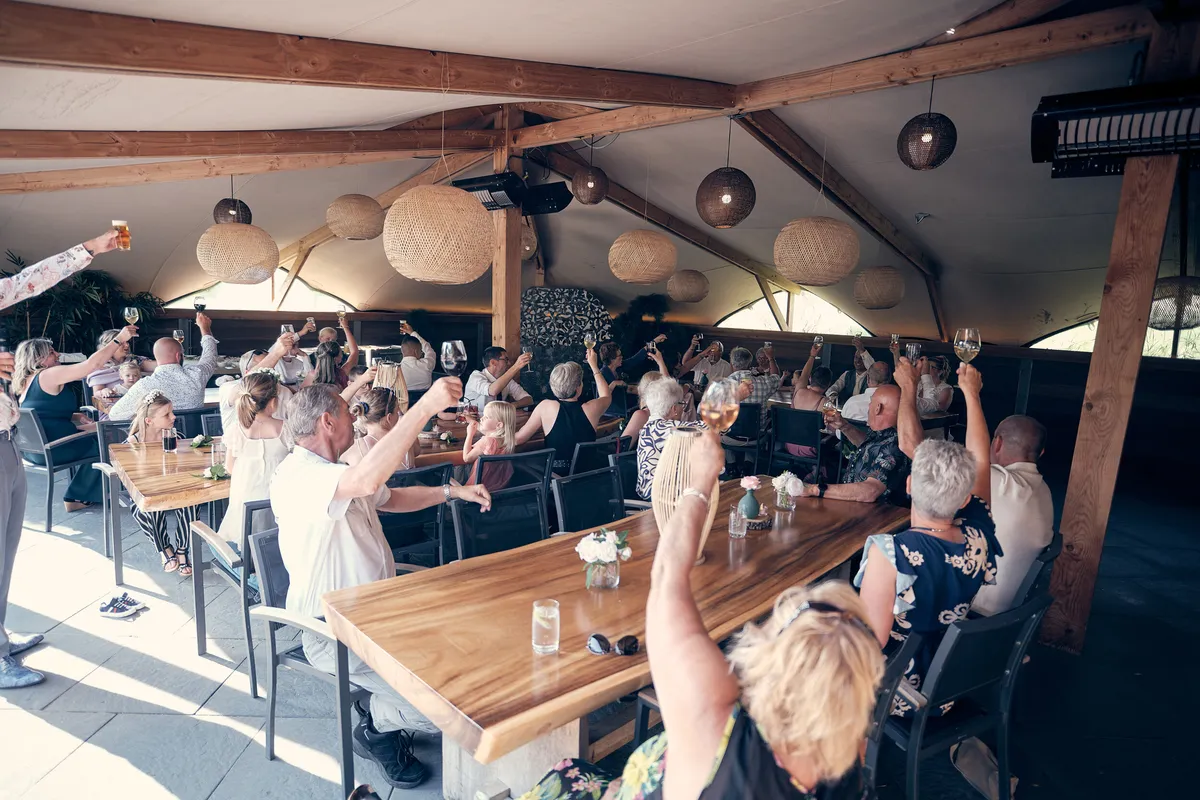 De gasten aan de lange houten tafels, met het bruidspaar in het midden
