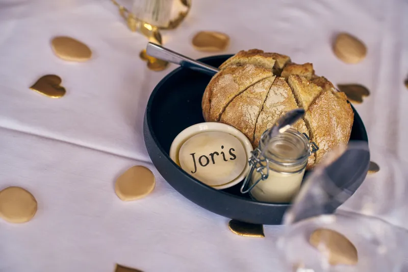 Een broodje met een naamkaartje bij het bord, met gouden confetti op tafel