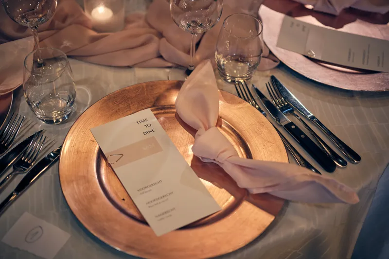 Een gedekte tafel met een gouden onderbord en een menukaart