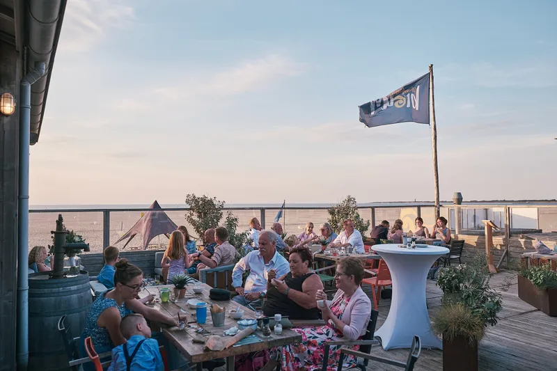 Gasten aan tafel op het terras van Brouw bij het eind van de middag