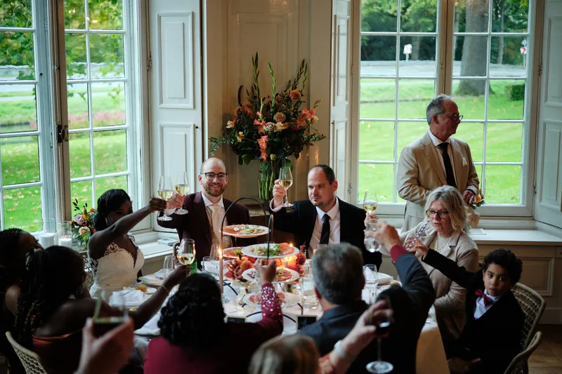 Gasten proosten aan tafel voor de hoge ramen