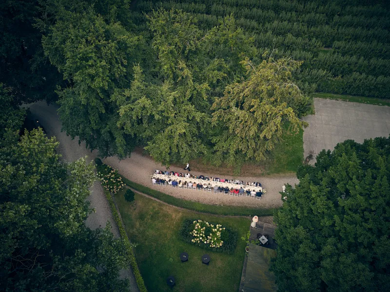 De lange tafel met alle gasten van bovenaf, tussen de bomen