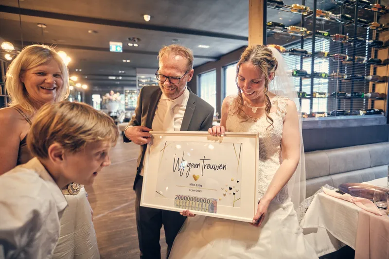 Mike en Ilja met het cadeau van de gasten: ingelijst geld onder ‘Wij gaan trouwen’; een jongen kijkt verrast