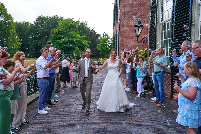 Rutger en Caroline lopen door een haag van gasten met bellenblazers