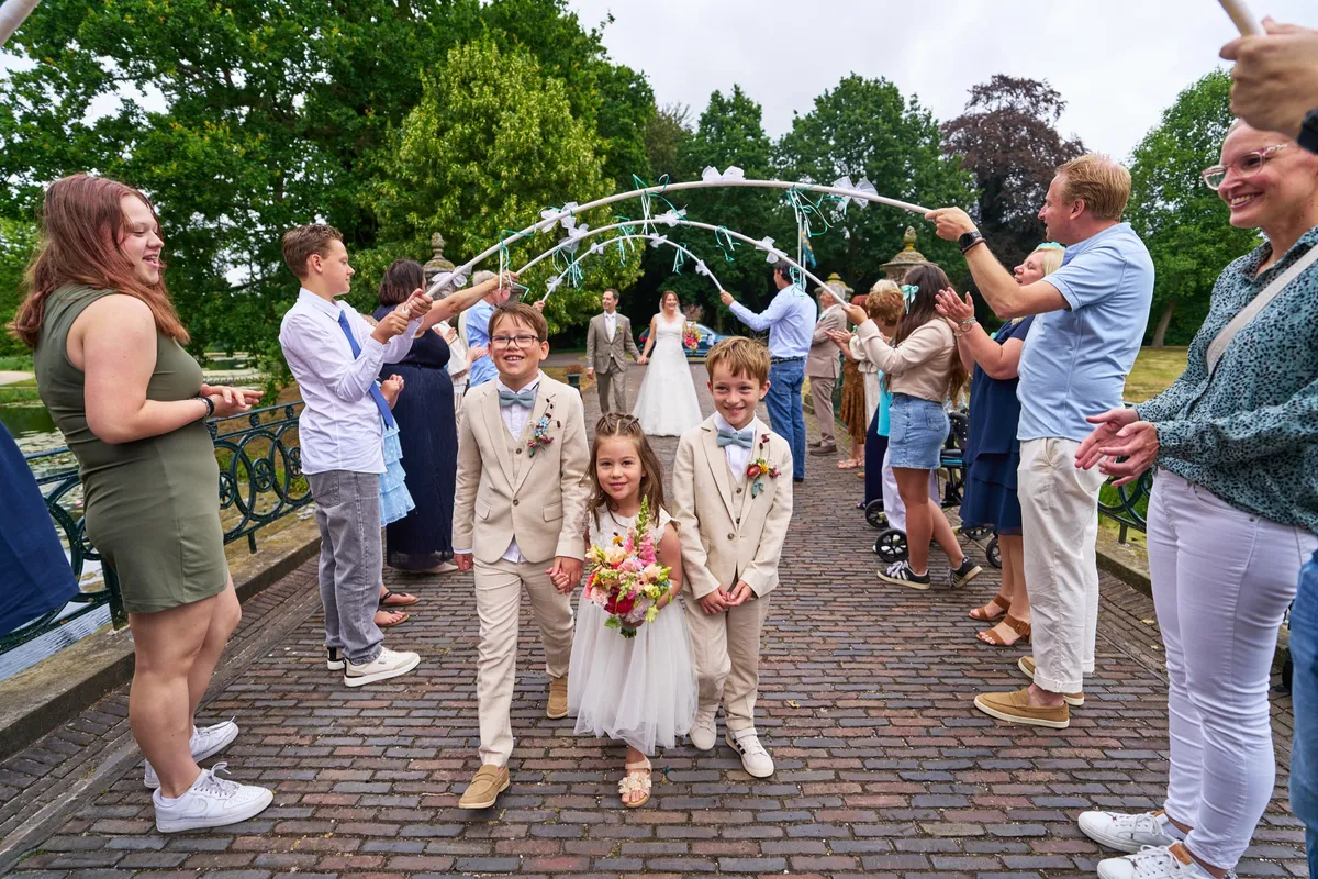 Gasten houden een boog van linten boven de brug, de kinderen lopen eronderdoor