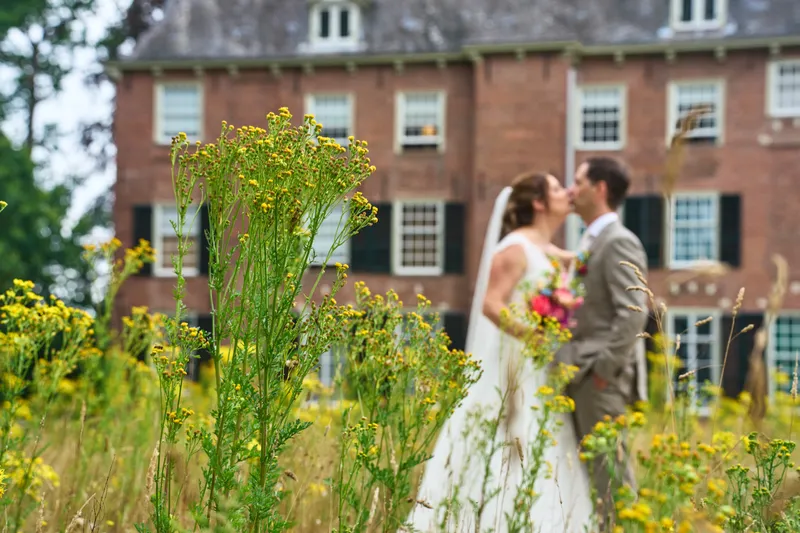 Rutger en Caroline kussen achter de gele bloemen, het kasteel onscherp erachter
