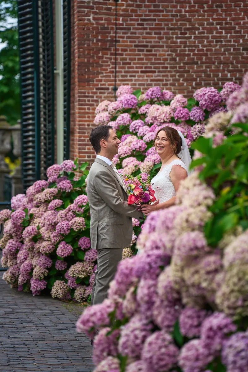 Caroline lacht tussen de roze hortensia’s tegen de muur