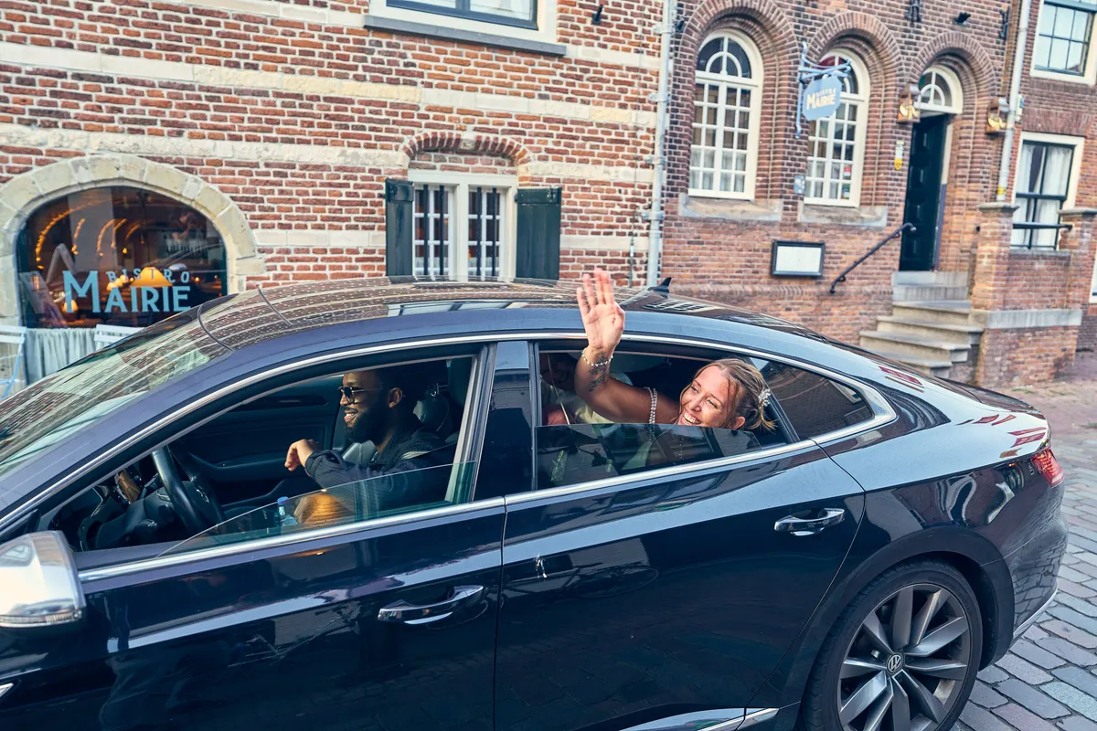 Diliana en Olav zwaaien uit het raam van de auto bij het vertrek
