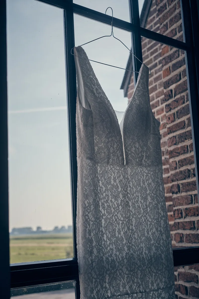 De trouwjurk hangt voor het raam met uitzicht over de polder