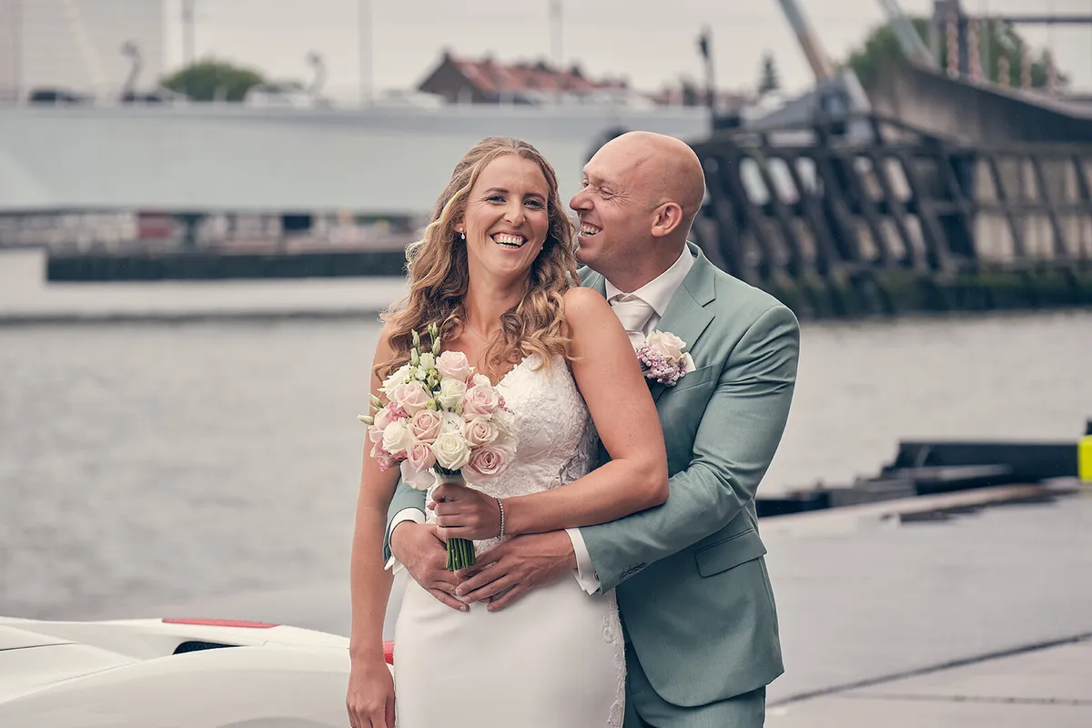 Het bruidspaar lacht aan het water op de Kop van Zuid