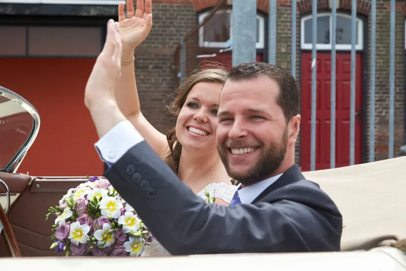 Robbert en Nadine zwaaien lachend uit de Porsche